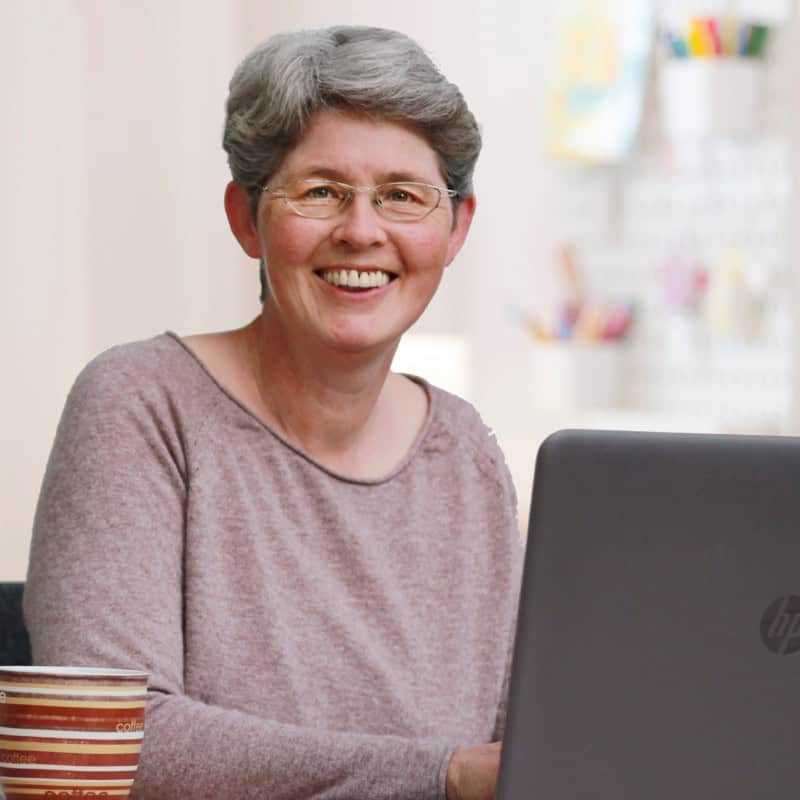 Claudia Barfuss, Webdesignerin in beigem Pullover an einem Tisch siztzend mit einem Notebook vor sich und links eine Tasse.