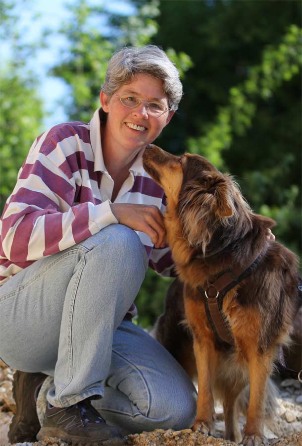 Claudia Barfuss kniet lächelnd neben ihrer Hündin Jenna, die sie ansieht.