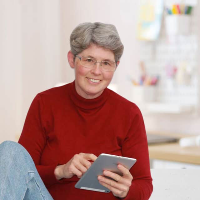 Porträtfoto von Claudia Barfuss, Webdesignerin für selbstständige Frauen sitzend, mit einem silbernen Tablet in der Hand