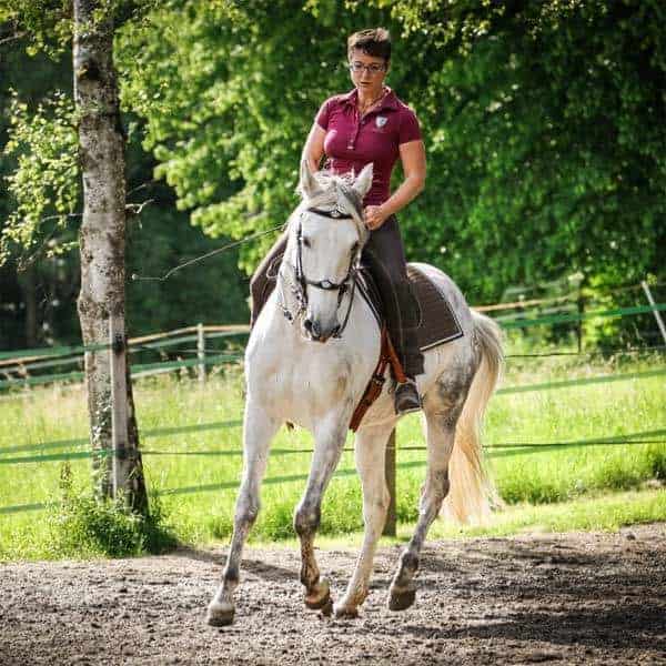 Lara Ree als Reiterin auf einem Schimmel im Galopp im Grünen.