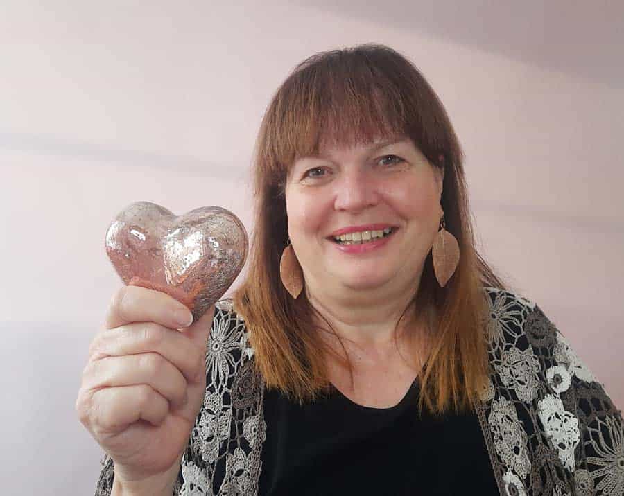 Portrait von Sabine Minister-Hellmayr die ein metallenes Herz hochhält.